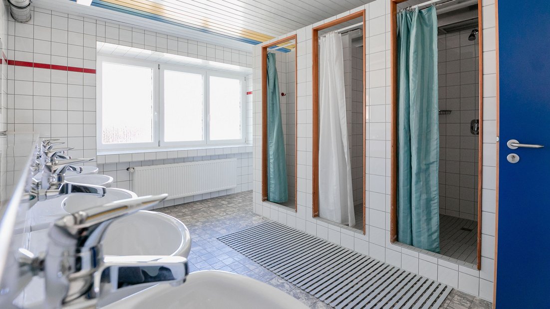 Baño de azulejos blancos en la casa de verano con múltiples lavabos y duchas