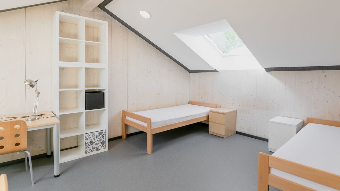 Habitación abuhardillada en el Rosenhaus con dos camas, estantería blanca y escritorio