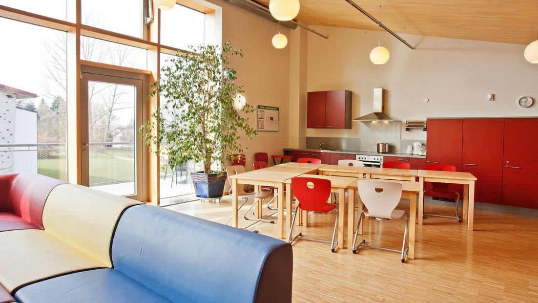 Zona común superior en el Wiesenhaus con balcón: con cocina roja, mesa de comedor y sala de estar en primer plano