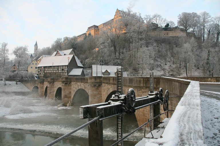 Vista de invierno hacia el puente de piedra con arcos de medio punto y presa en el Schloss-Berg Kirchberg